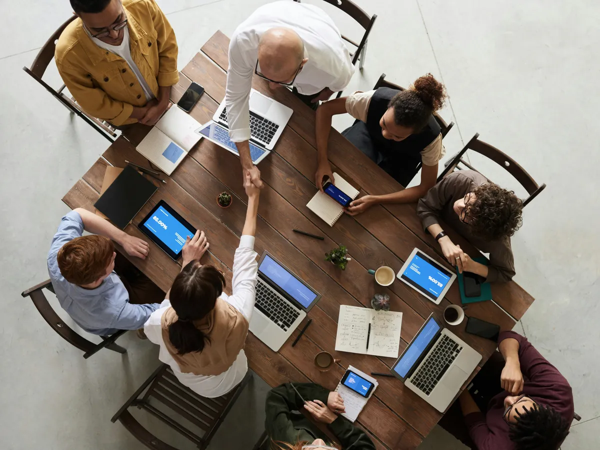 Equipo diverso colaborando alrededor de una mesa con laptops, vista cenital